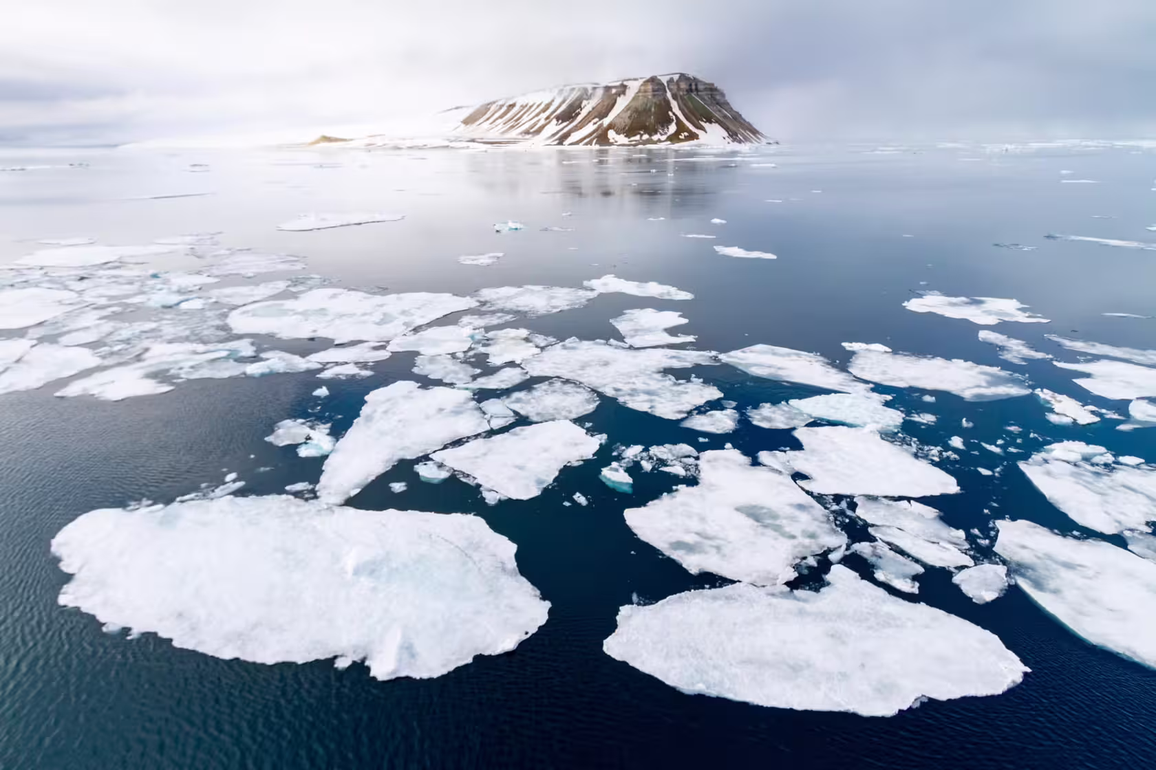 Vista aérea de bloques de hielo flotando en el mar, con una isla al fondo