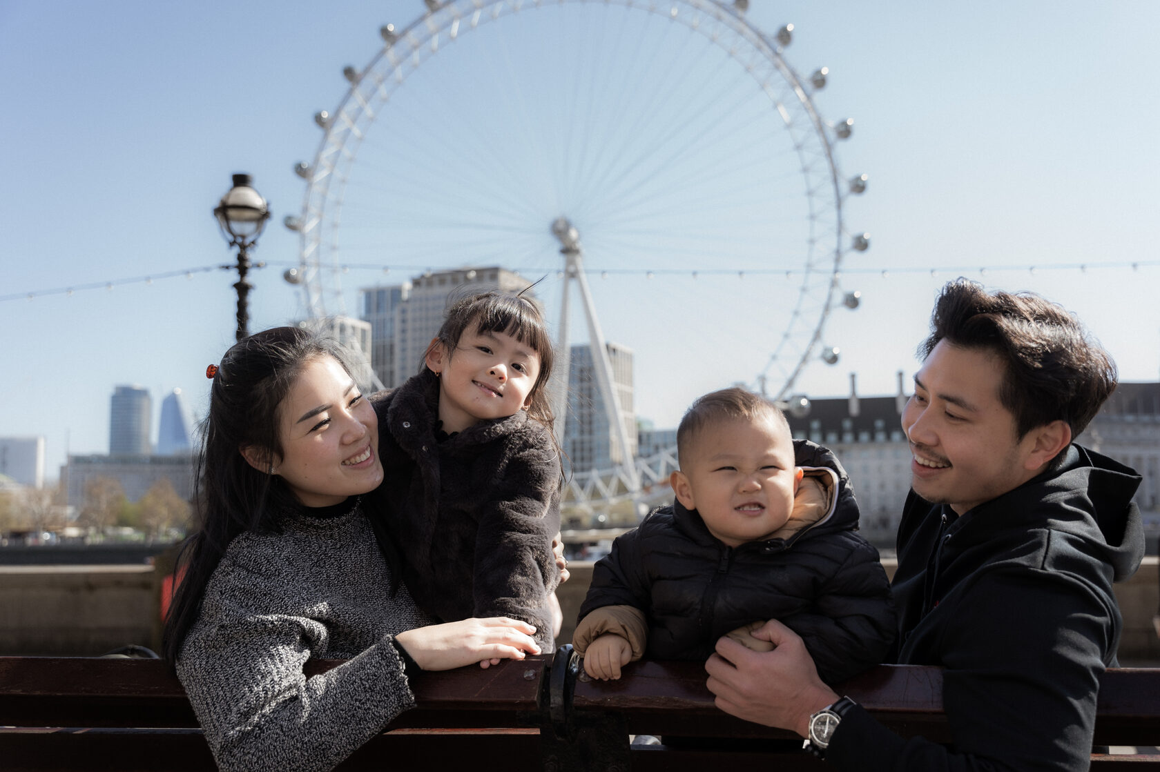 Family smiling together beside the Thames with the London Eye behind them