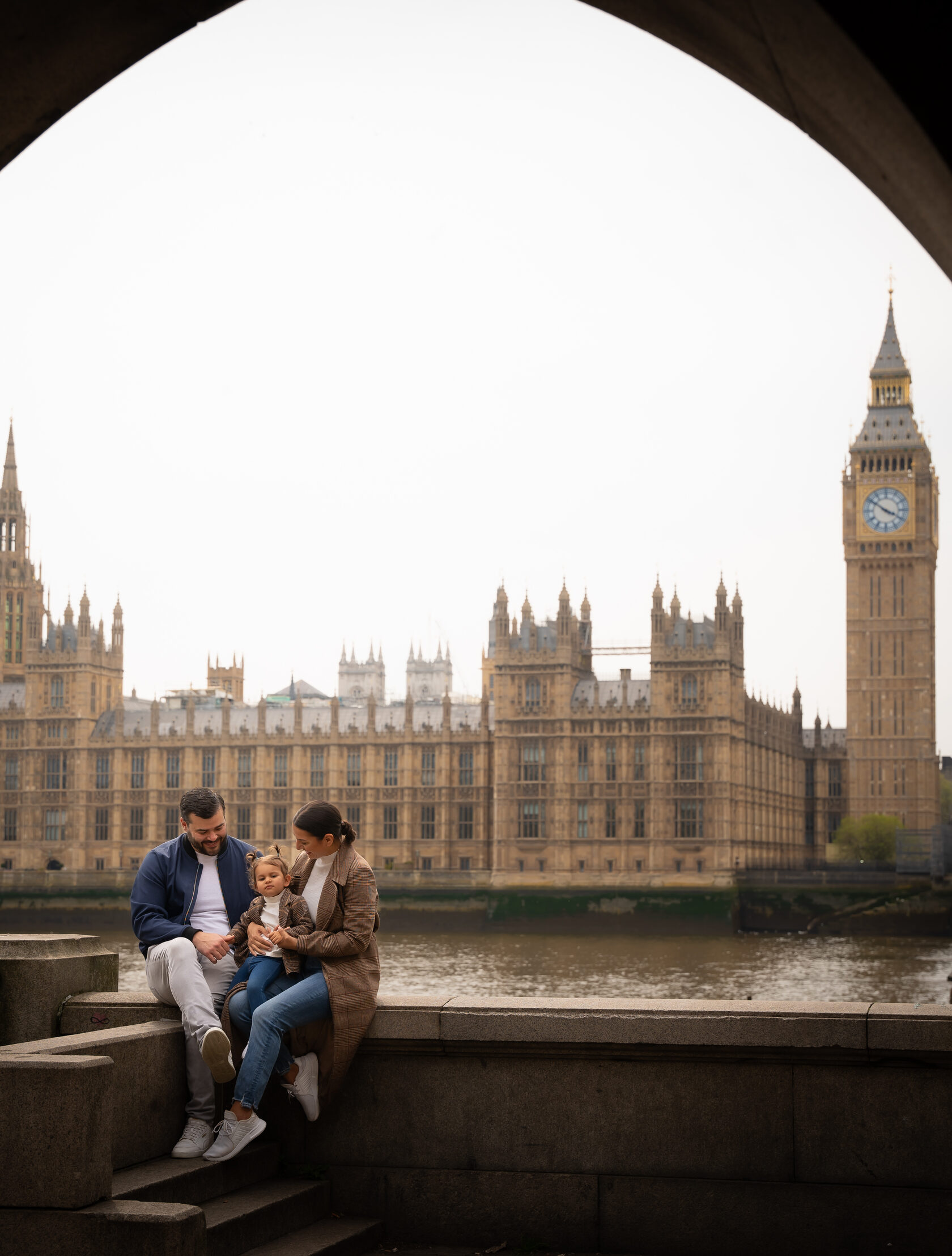 Parents and toddler beneath an arch overlooking Parliament