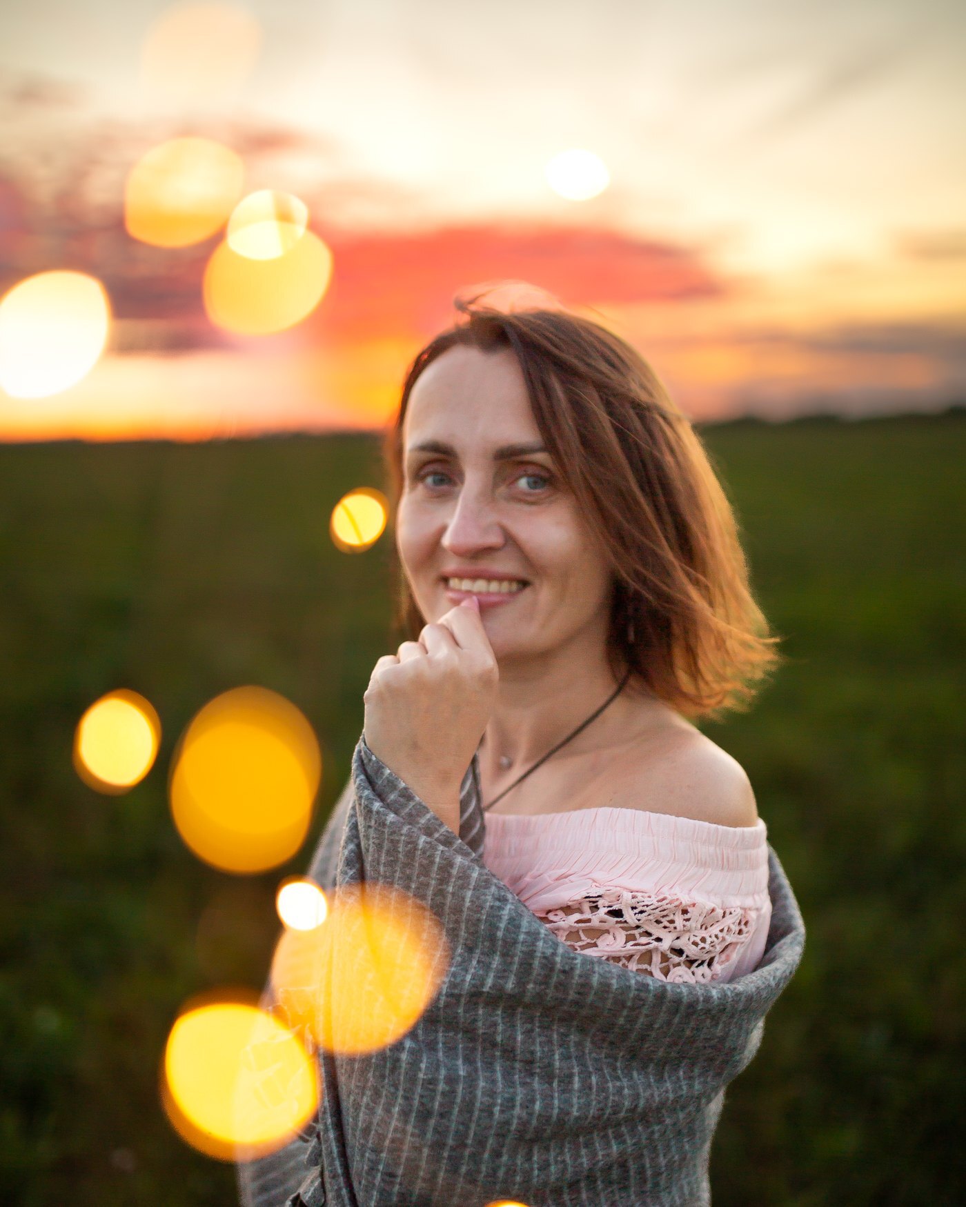 A woman in a field at sunset with bokeh lights