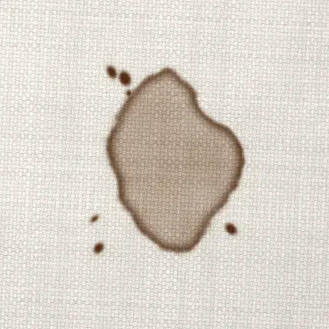 Symbolbild: eingetrockneter Kaffeefleck mit braunem Rand auf hellem Sofastoff in Nahaufnahme. Solche Gerbstoff-R&auml;nder behandelt Shikardos Reinigung in Frankfurt vor und sp&uuml;lt die ganze Fl&auml;che.