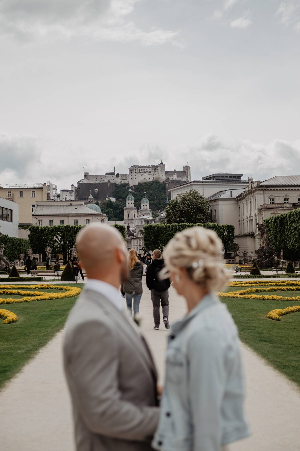 Bride and groom in the Mirabell Gardens in Salzburg, with the historic Hohensalzburg Fortress overlooking the city.