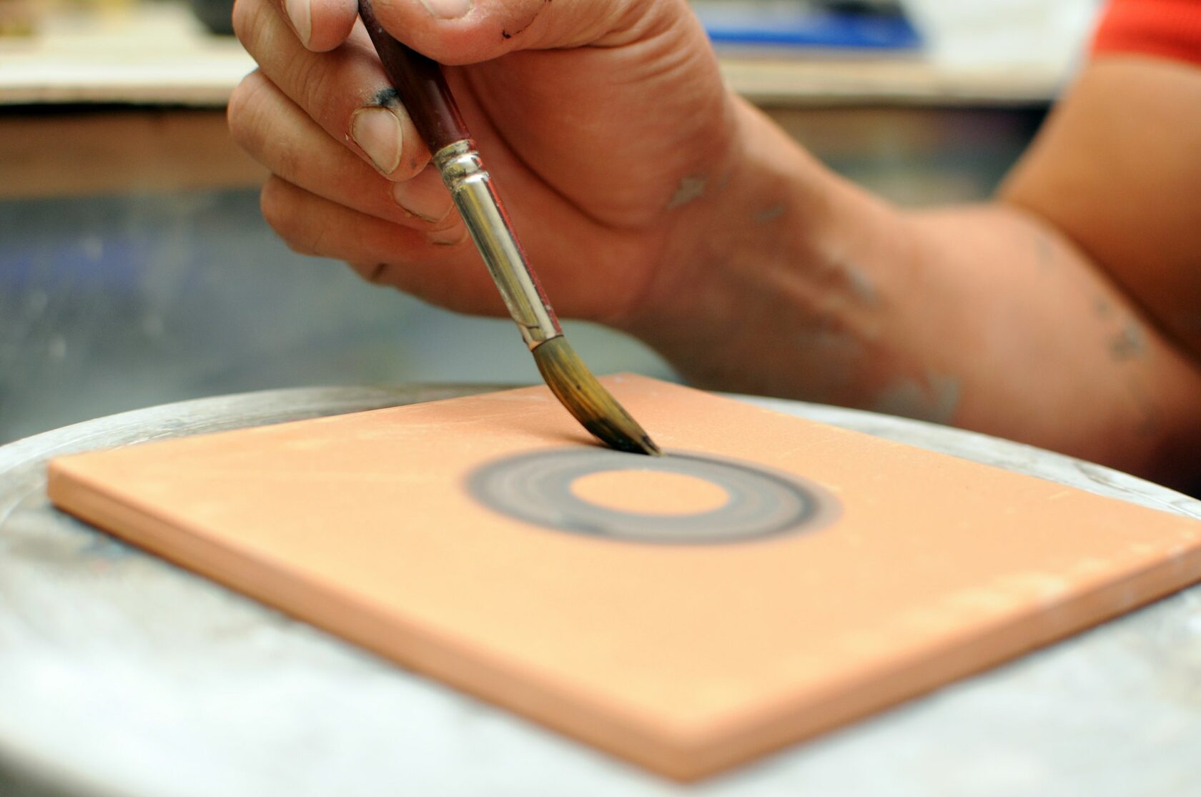 Close-up of hands painting a blue and white azulejo tile with a fine brush in a sunlit workshop