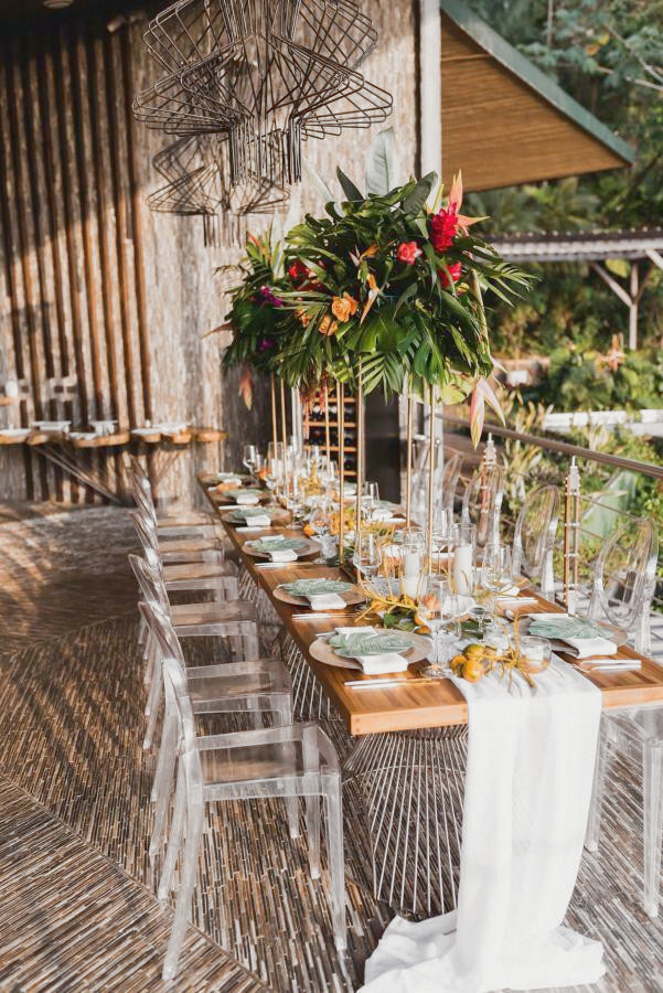 larga mesa de boda con flores tropicales y sillas transparentes en Makanda by the Sea