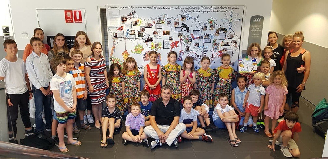 Romashka children, parents and teachers in front of the school map mural