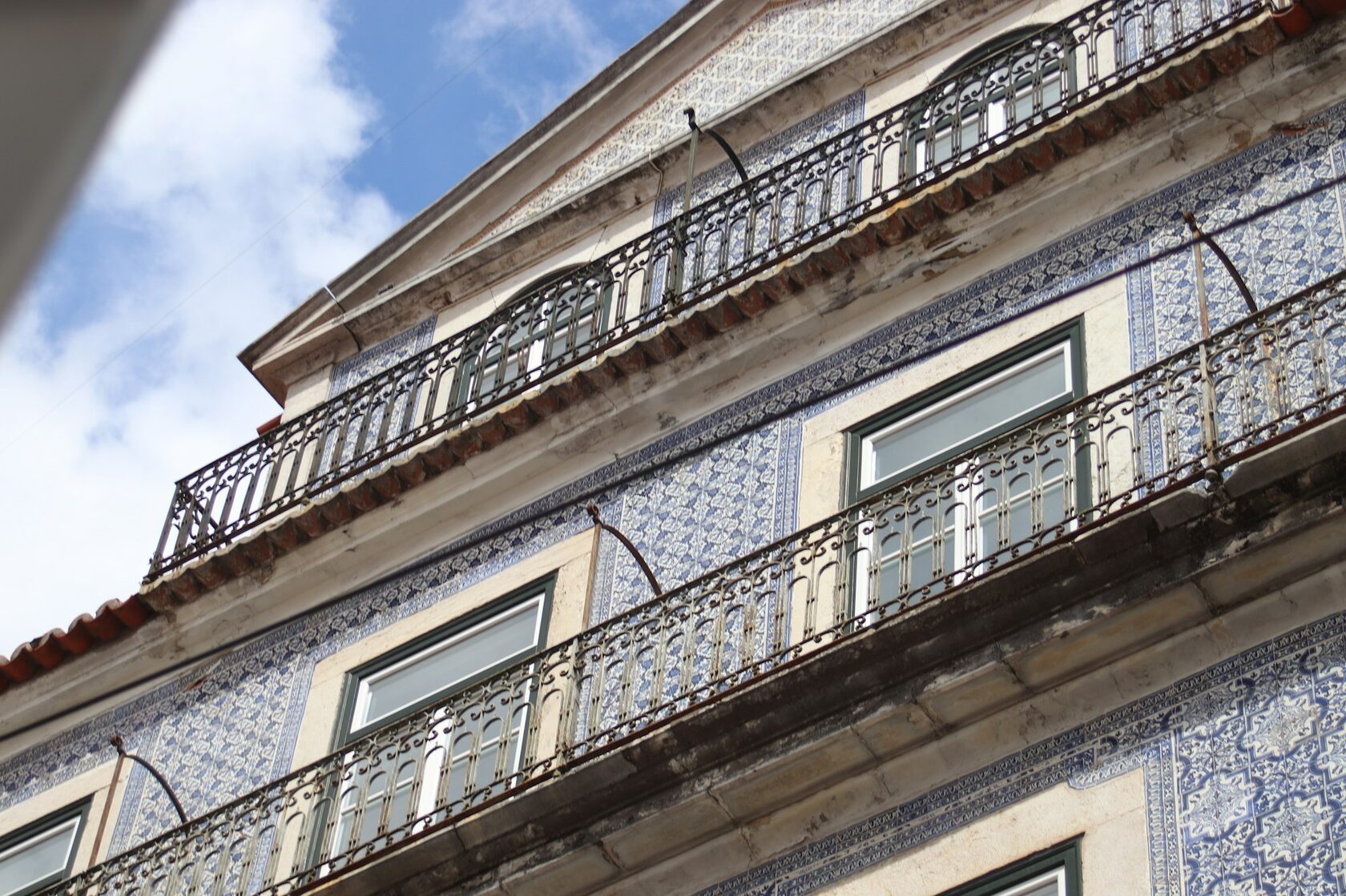 Hand-painted blue and white azulejo tiles on an old Lisbon facade, with a wrought-iron balcony and flowers above