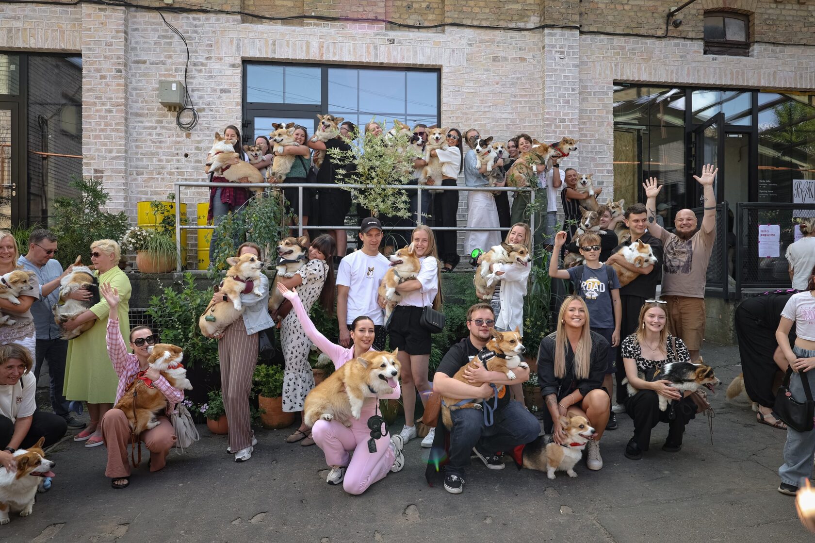 Group photo of people holding their corgis in front of a brick building at Corgi Fest Riga