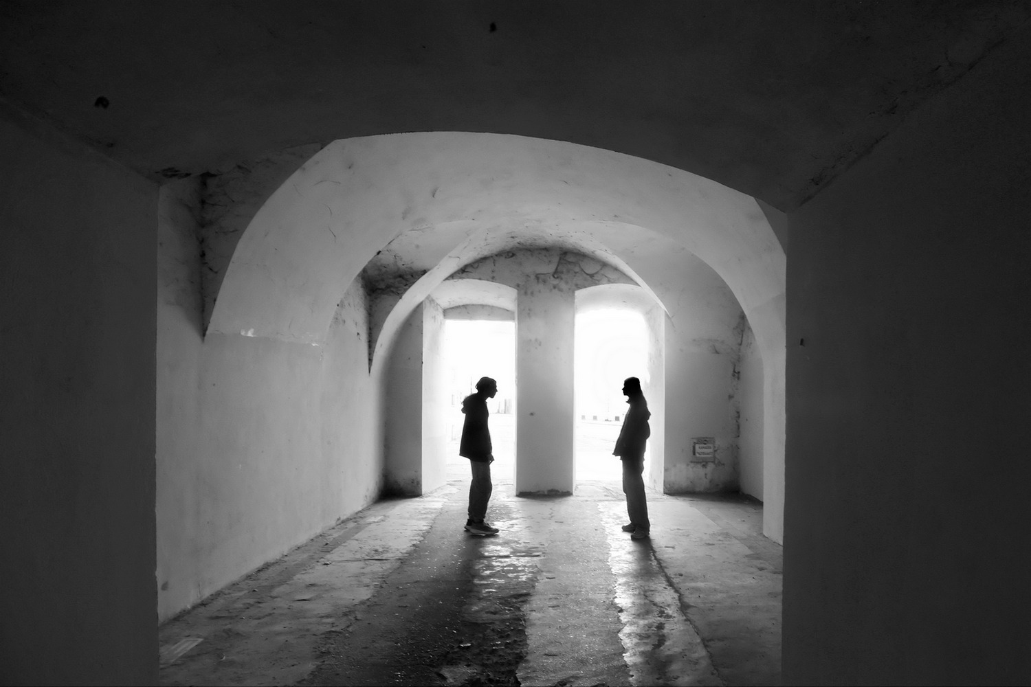 Two silhouettes standing in an arched white corridor