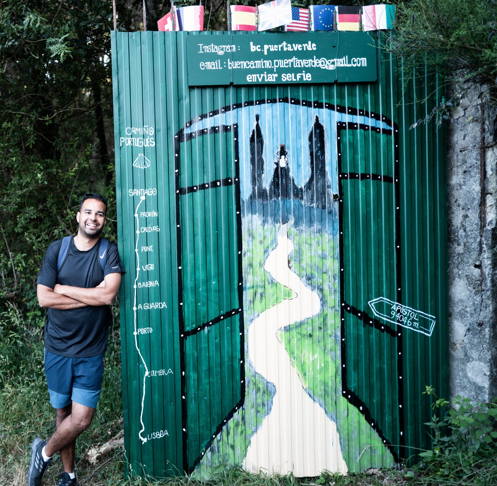 A painted Camino de Santiago waymark on a green fence beside a country path