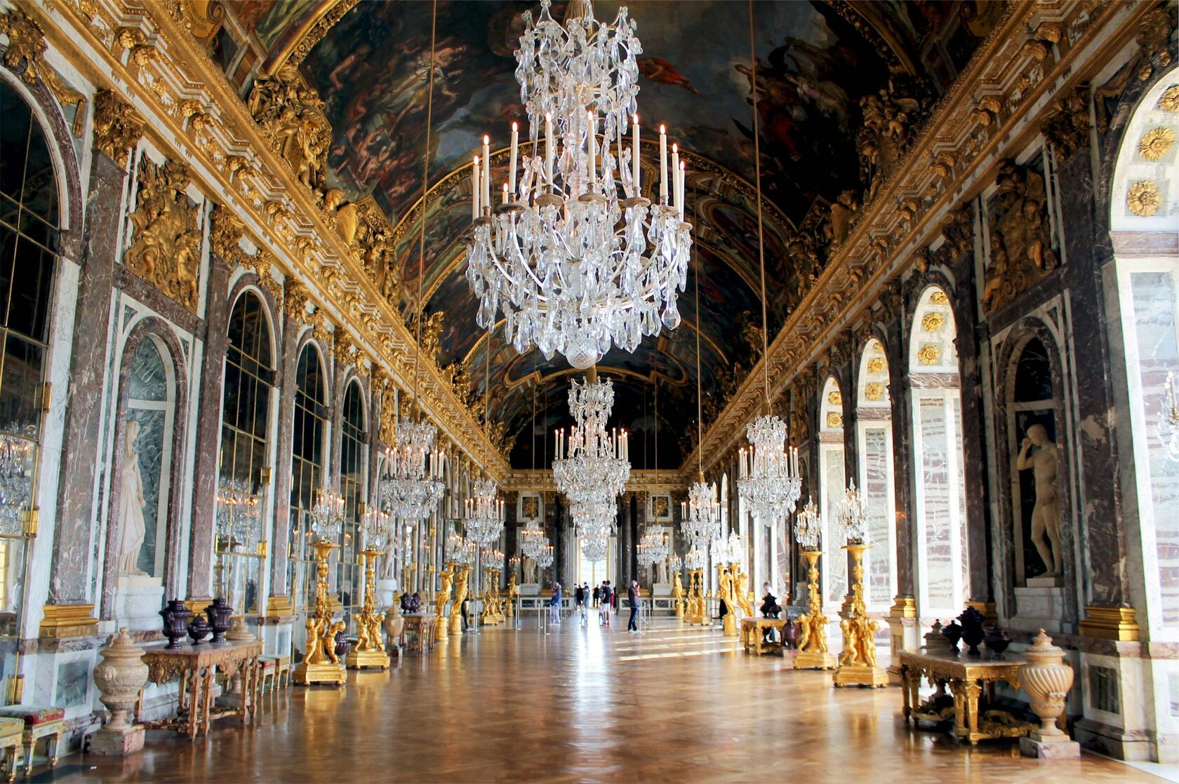 The Hall of Mirrors at the Palace of Versailles with chandeliers glowing above the parquet floor