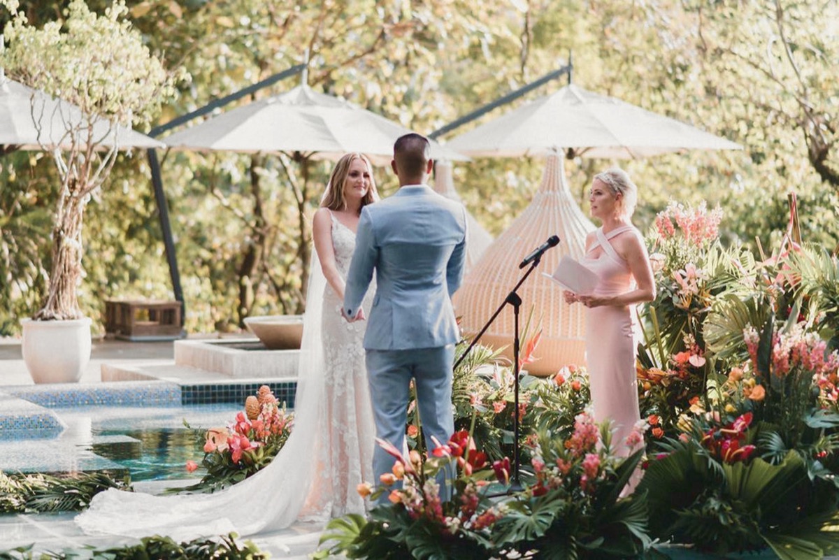 la pareja y el oficiante en el podio de flores de la ceremonia junto a la piscina principal, durante una reserva total de Makanda by the Sea