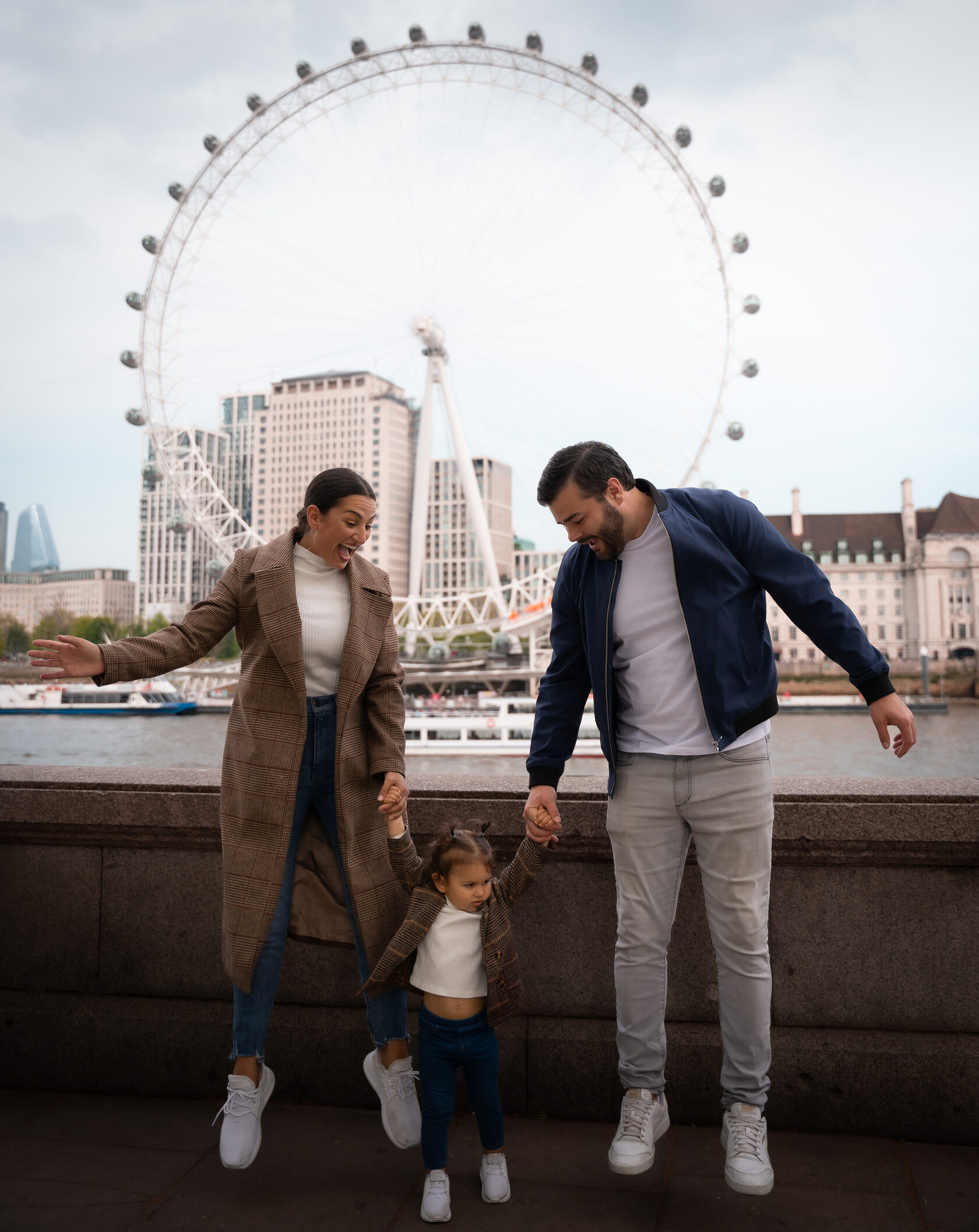 Parents holding their toddler’s hands with the London Eye behind them