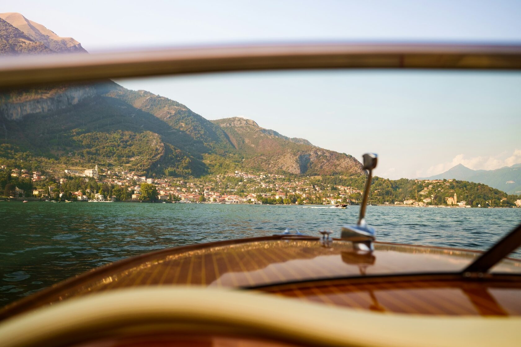 A classic wooden private boat cruising Lake Como past elegant lakeside villas