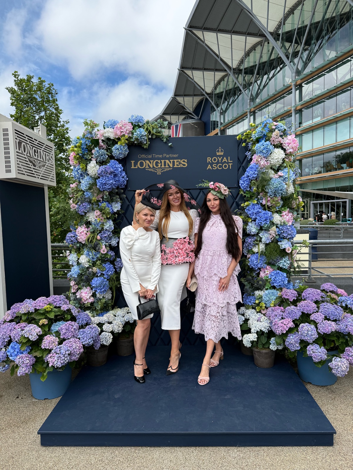 Три участницы поездки в шляпках у цветочной арки Royal Ascot