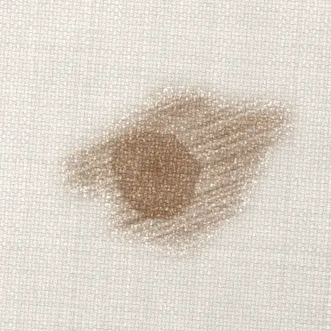 Symbolbild: verriebener Kaffeefleck mit Wischspuren und aufgerauter Faser auf hellem Sofastoff in Nahaufnahme. Shikardos Reinigung aus Frankfurt r&auml;t: tupfen, nicht reiben.