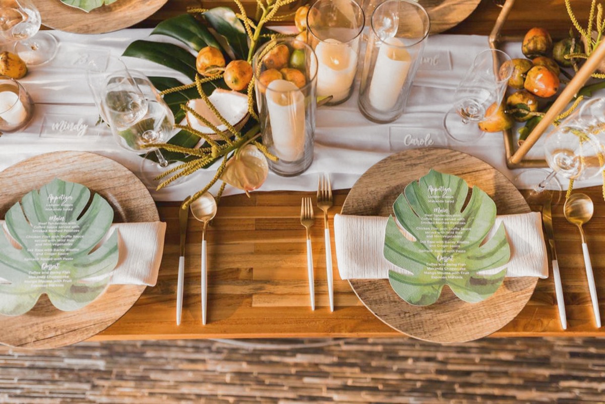 mesa tropical con menús en hojas de monstera en la recepción de una boda en Makanda