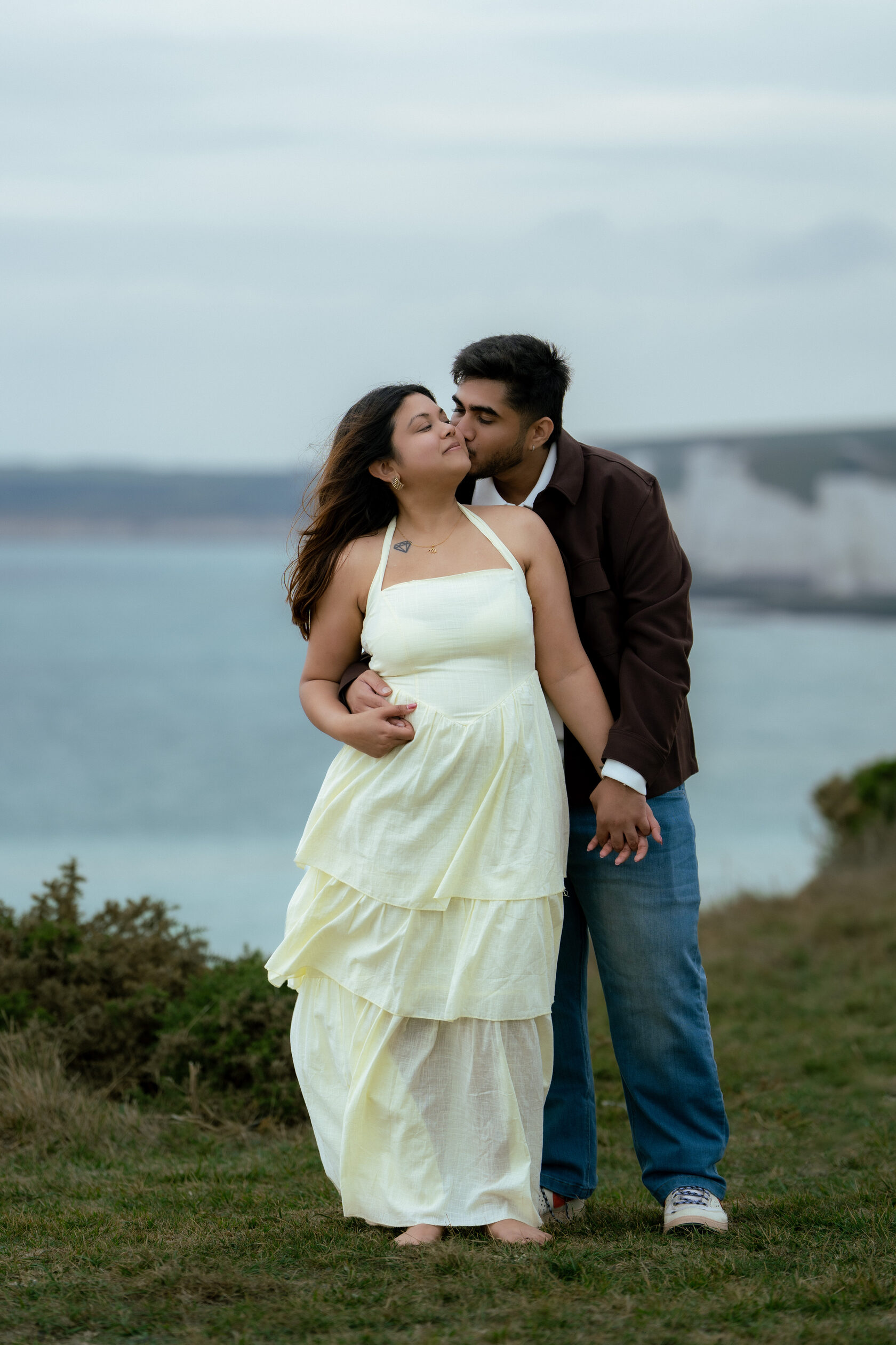 Couple standing together in a pale dress and dark jacket by the Sussex coast