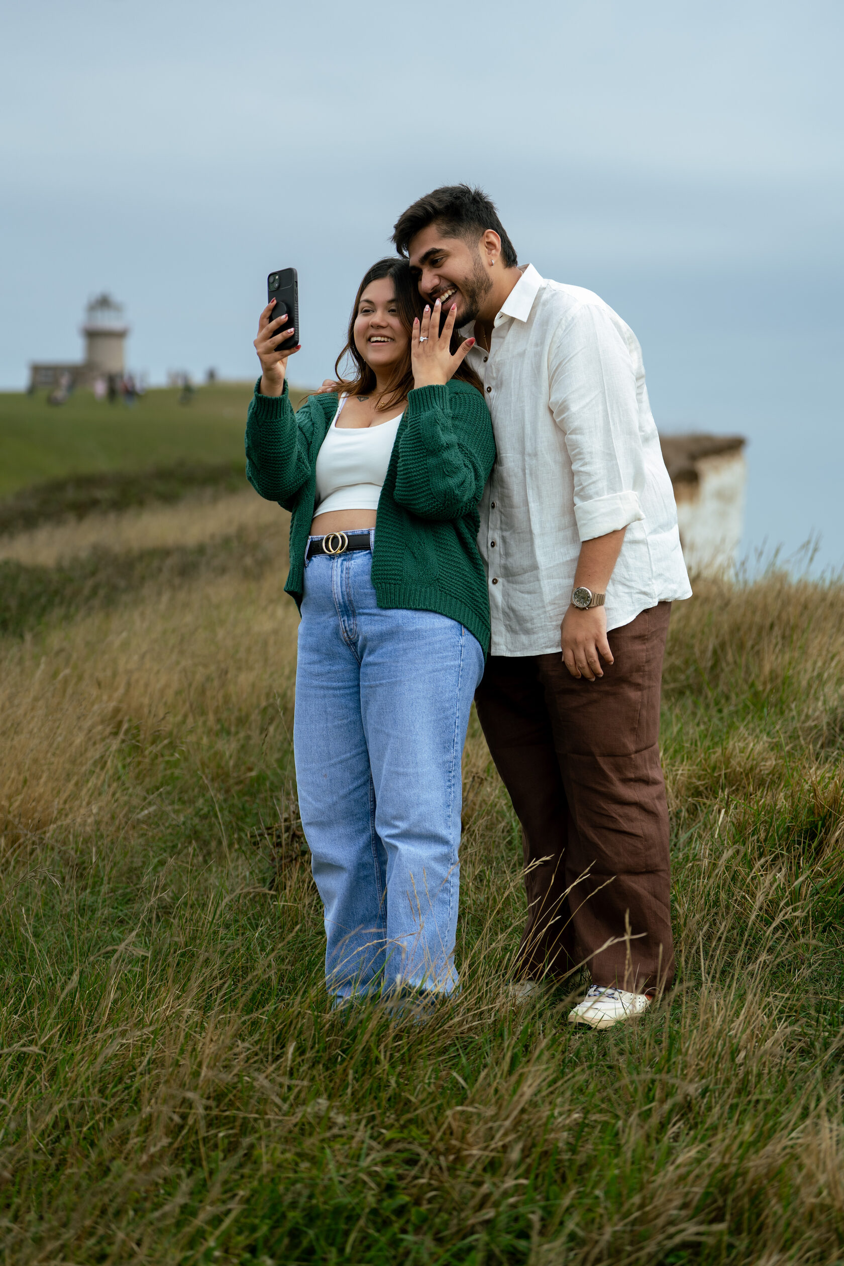 Newly engaged couple sharing a moment with a phone on the Sussex coast
