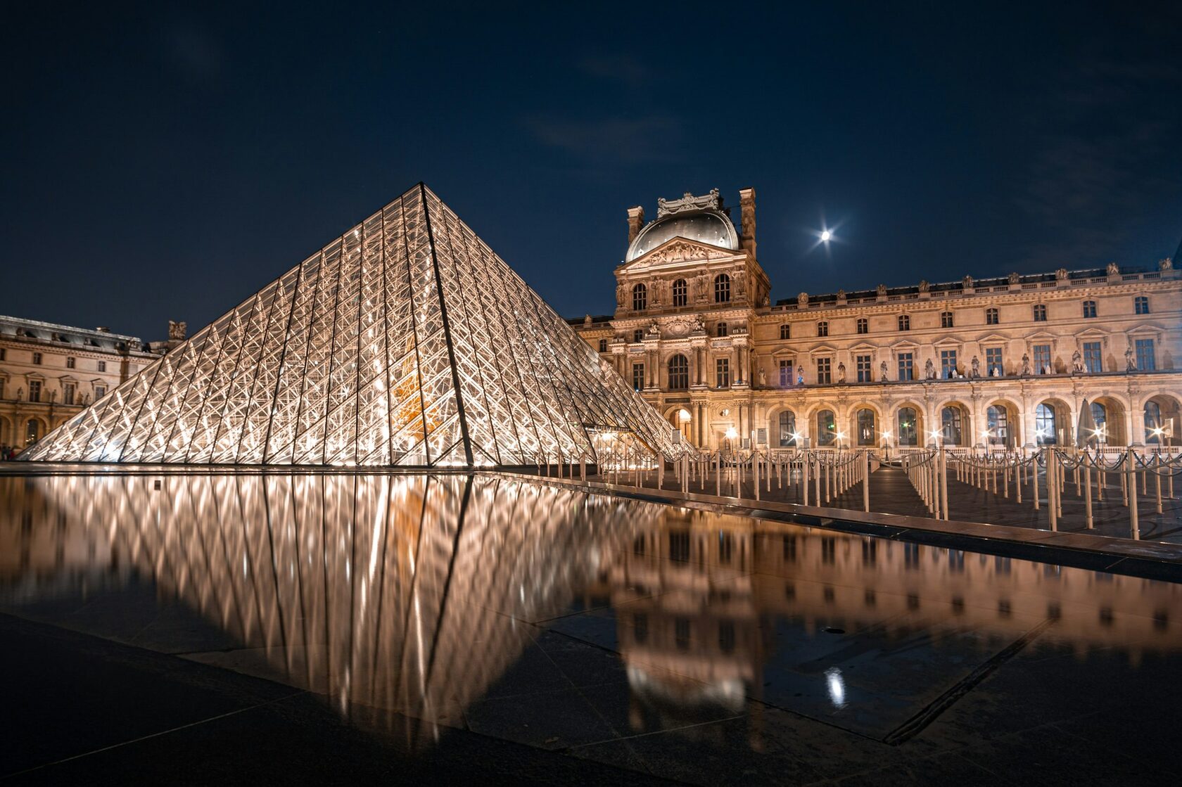 The Louvre's glass pyramid glowing at blue hour with the palace lit behind it