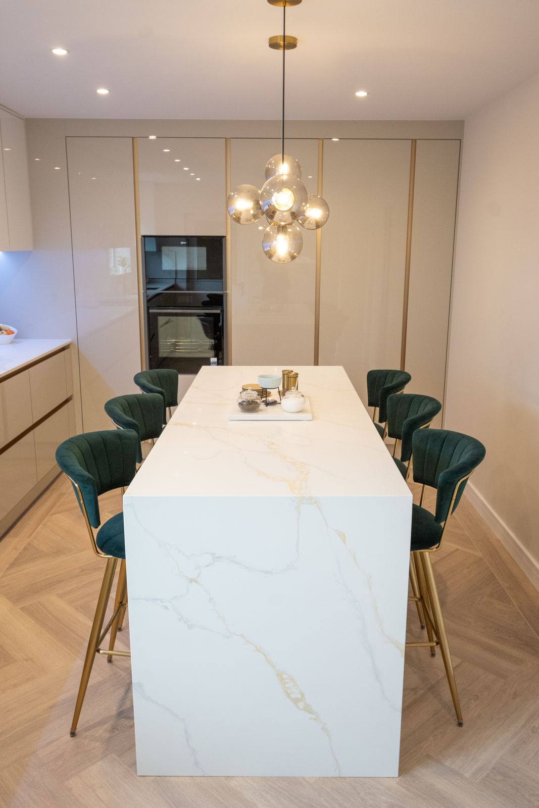 Handleless gloss kitchen with marble-effect waterfall island, green velvet stools and gold pendant light