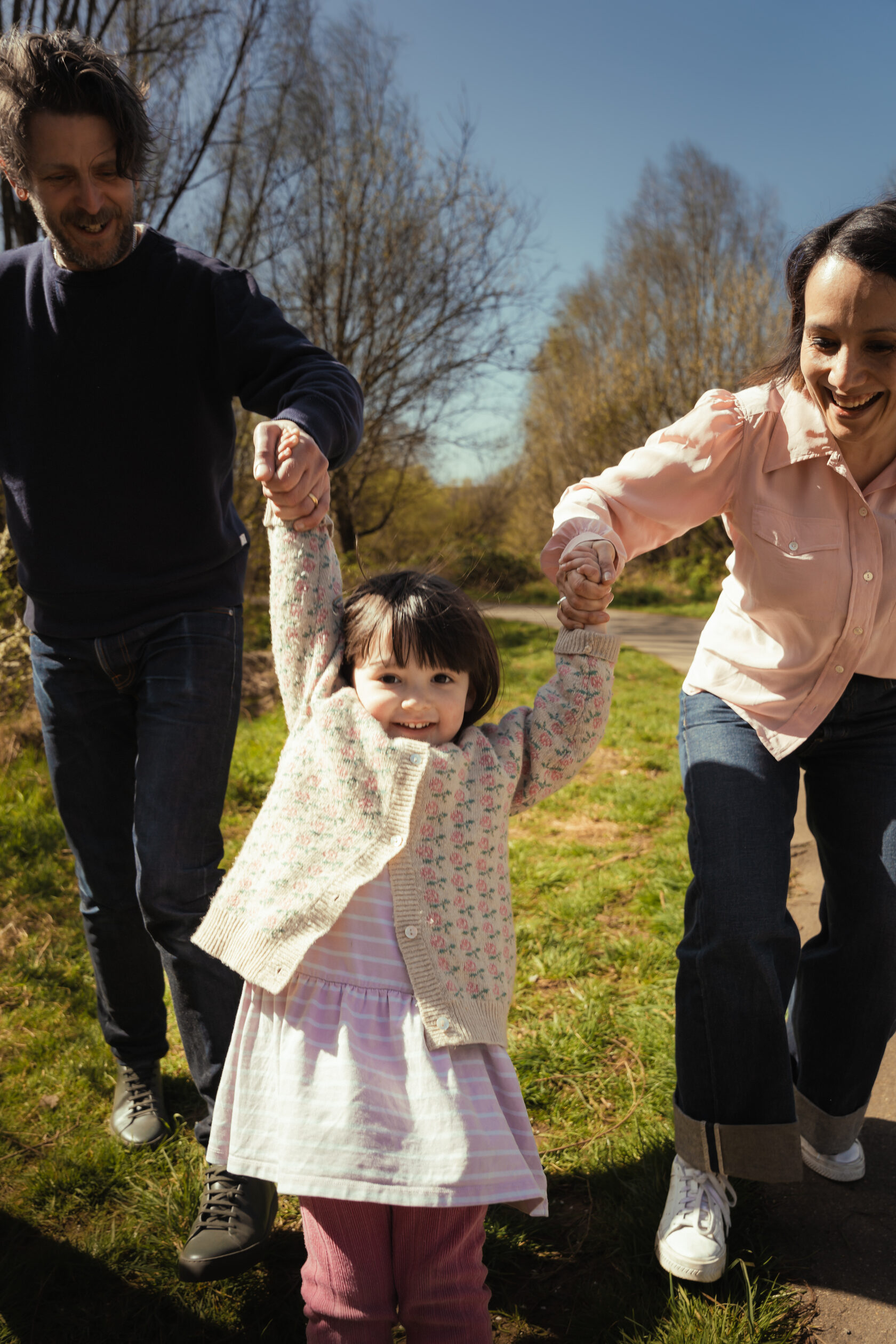 Child walking between parents on a grassy park path