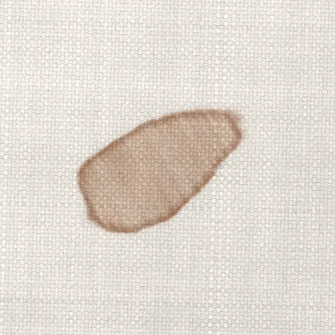 Symbolbild: eingetrockneter Make-up-Fleck mit Rand auf hellem Sofastoff in Nahaufnahme. Pigmente und Fett l&ouml;st Shikardos Reinigung in Wiesbaden mit Vorbehandlung und Absaugung.