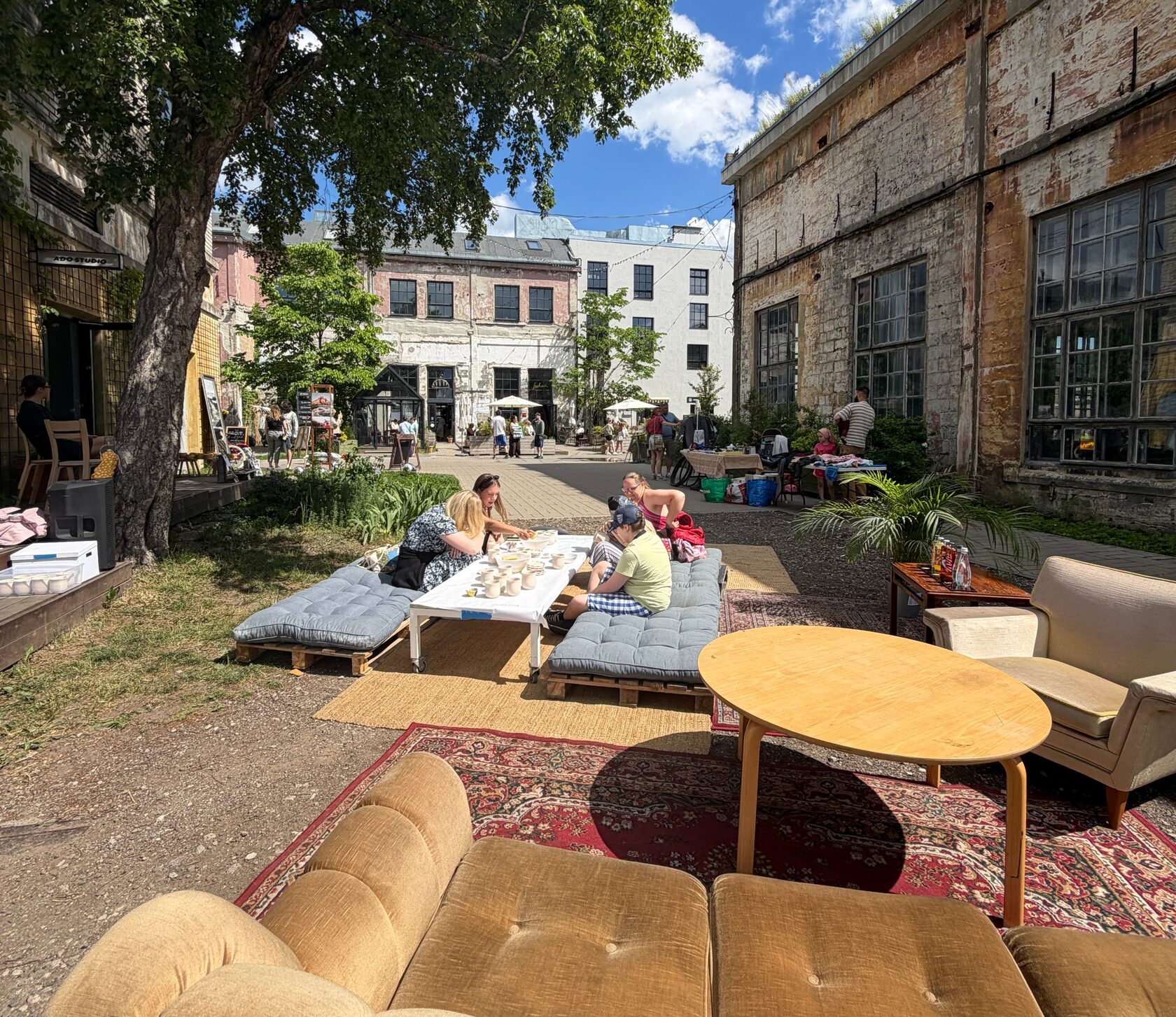 Old sofas, rugs and a ceramics workshop table set up in a sunny factory courtyard at sofa häng