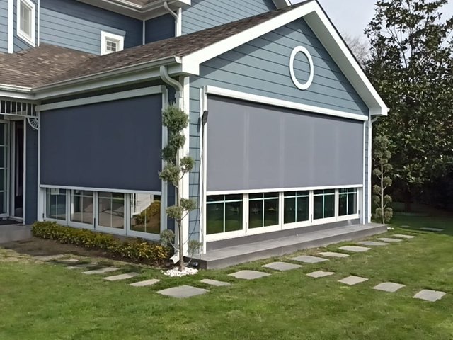 VITOZIP zip screen lowered over a window wall of a blue house