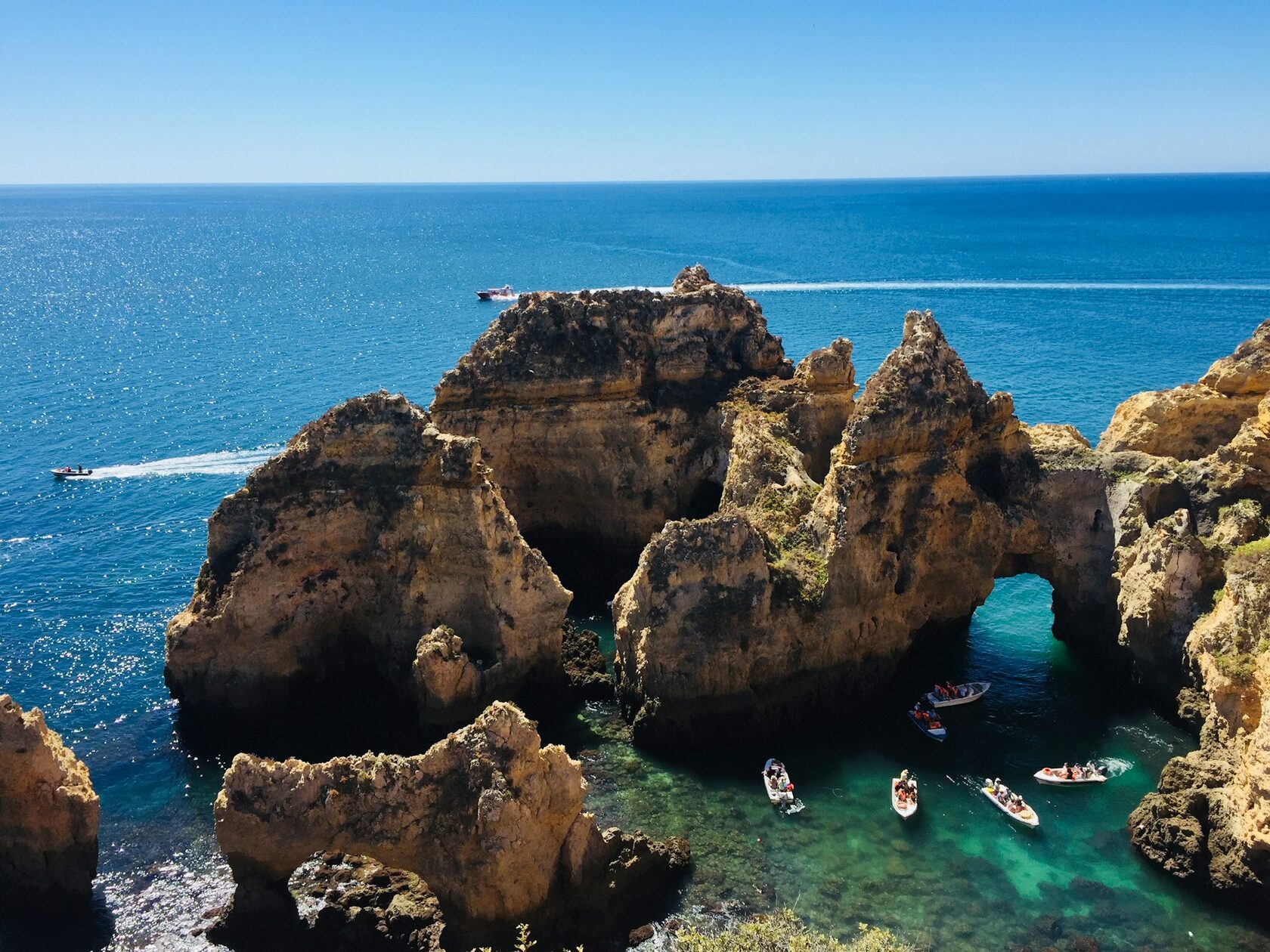 A white catamaran sailing past golden Algarve cliffs on a bright, calm day