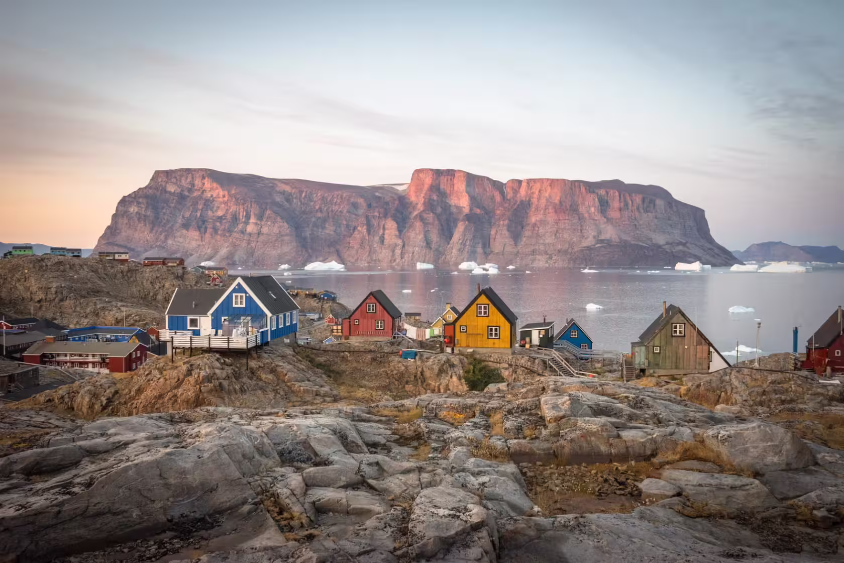 Casas de colores junto a un fiordo de Groenlandia, con grandes acantilados de roca rojiza al atardecer