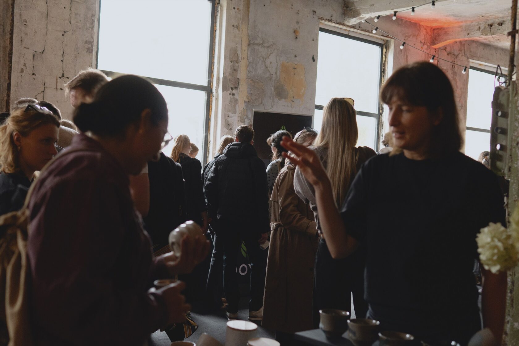 Visitors browsing a ceramics stall in a bright factory hall at a Põhjala market