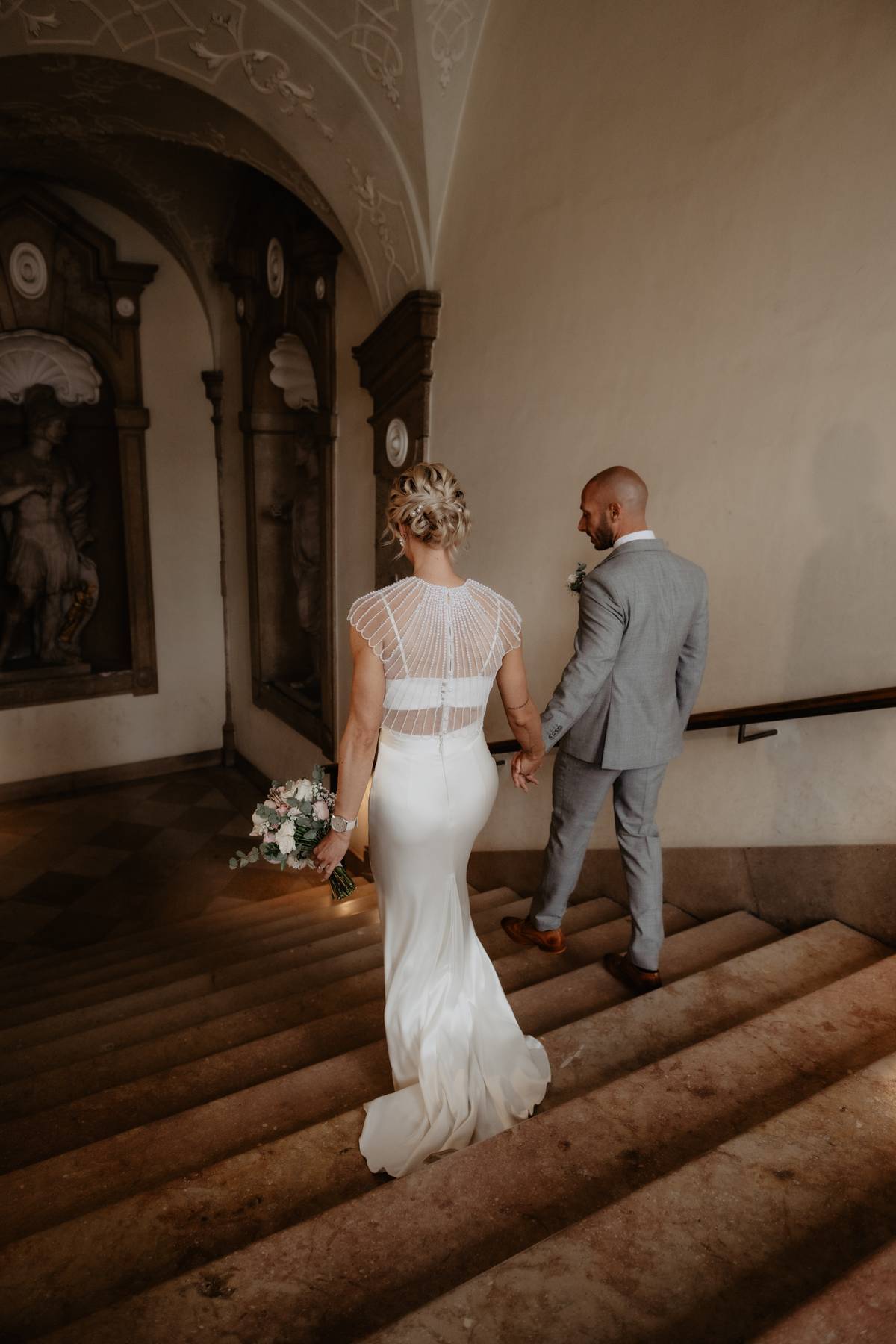 Bride and groom walking hand in hand down the historic staircase of Schloss Mirabell in Salzburg after their civil wedding ceremony.