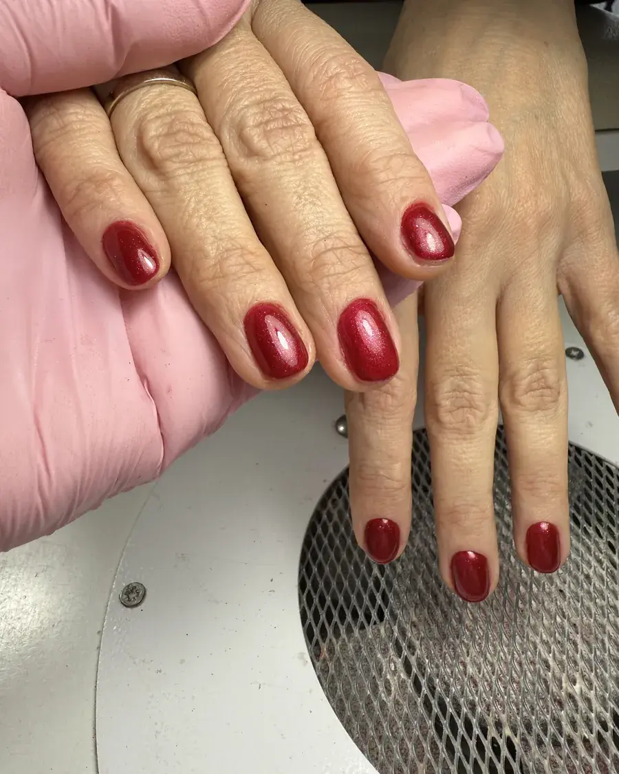 Short nails in glossy deep red gel, shown on a client's hand