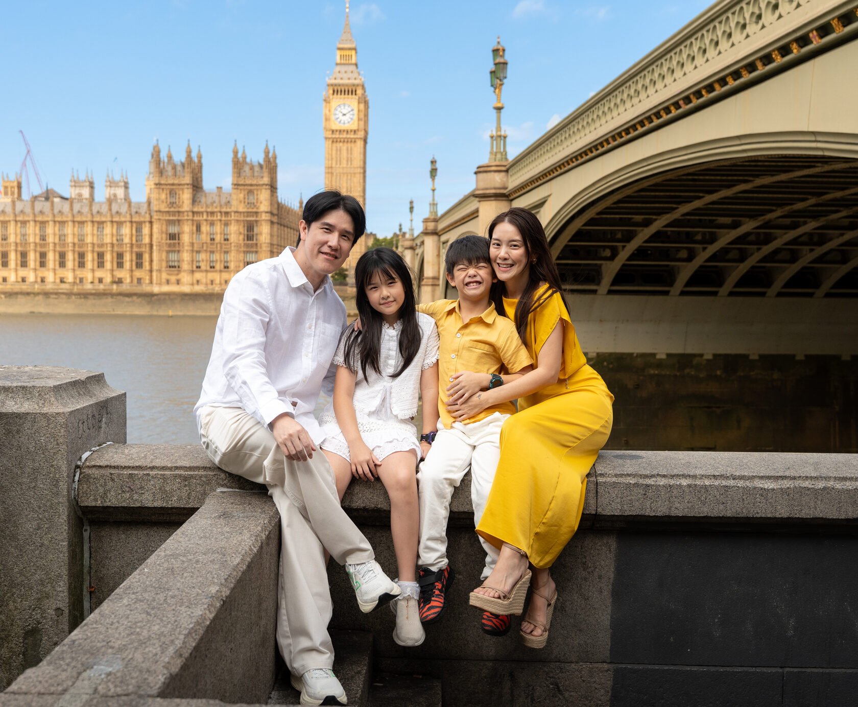 Family seated together beside Westminster Bridge