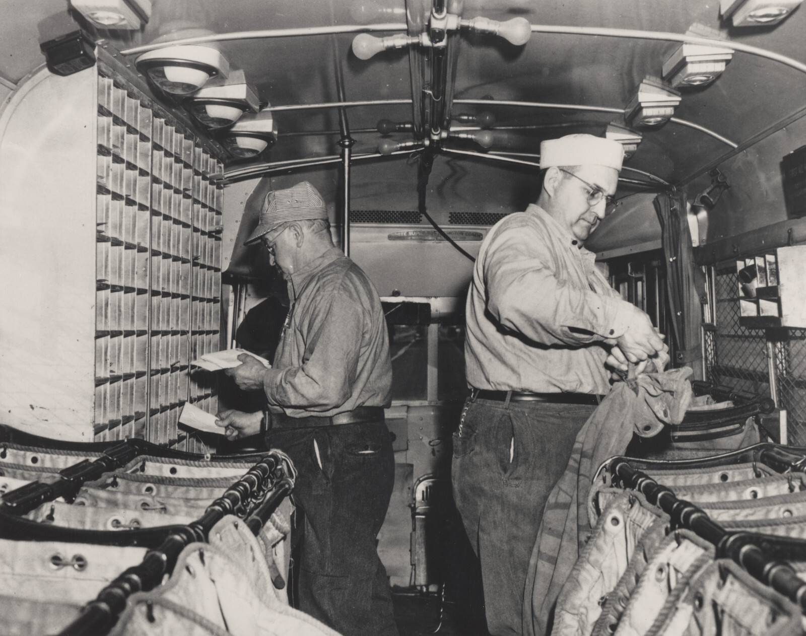 Archive photograph of postal clerks sorting letters by hand inside a Highway Post Office bus