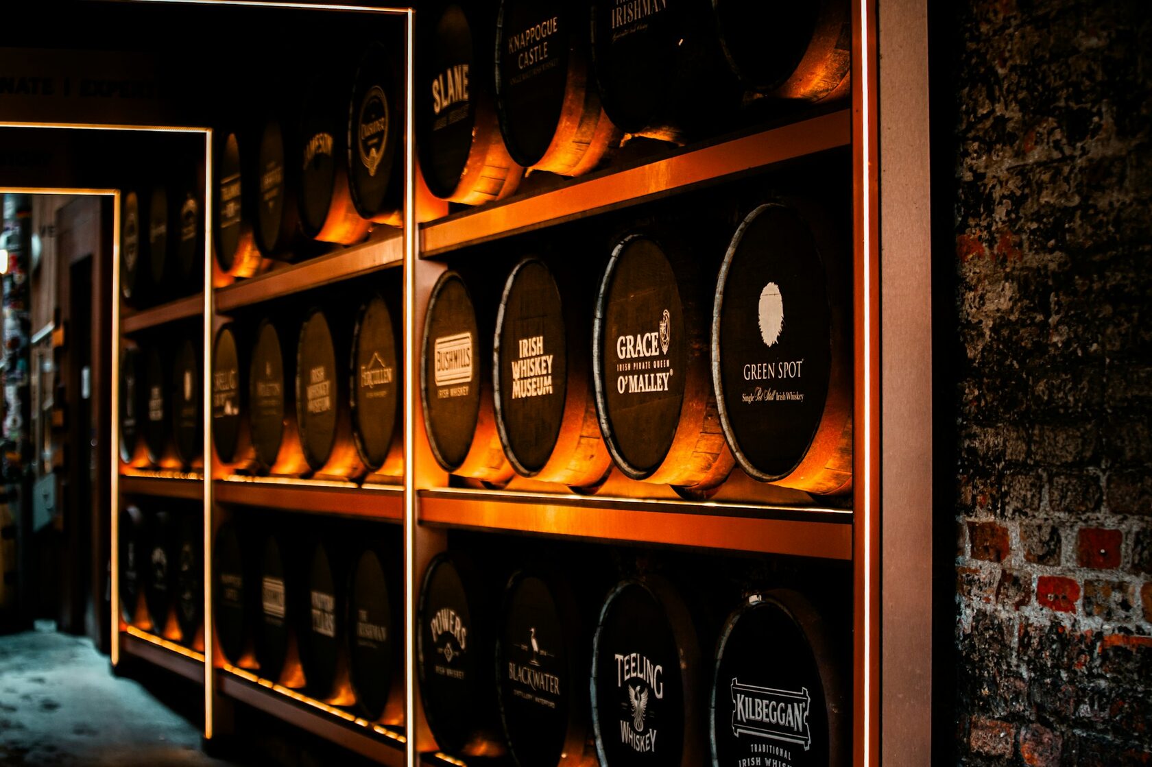 Rows of oak whiskey barrels in a dim stone warehouse, a glass of golden whiskey resting on a cask, warm light.