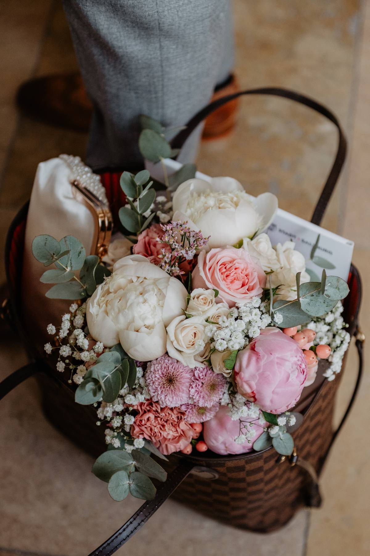 Romantic bridal bouquet with blush pink roses, white peonies and eucalyptus, resting in a wicker basket.