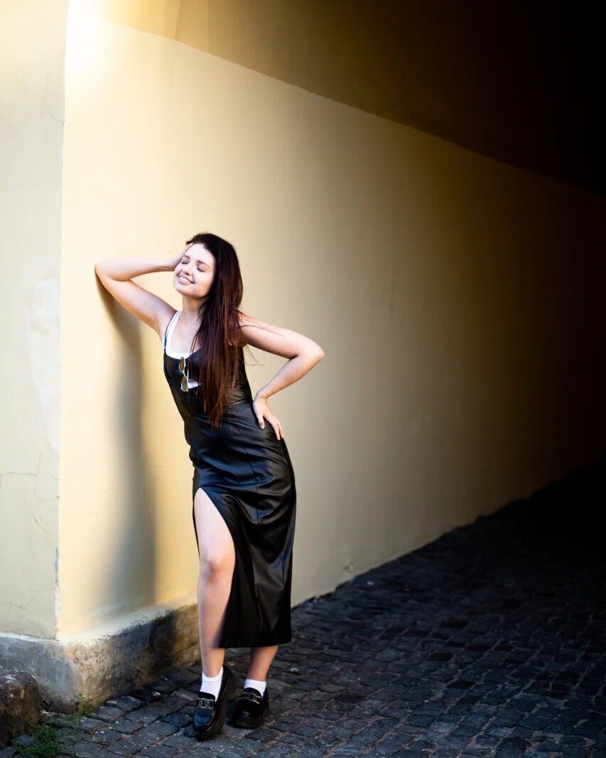 A woman in a black slip dress against a sunlit wall