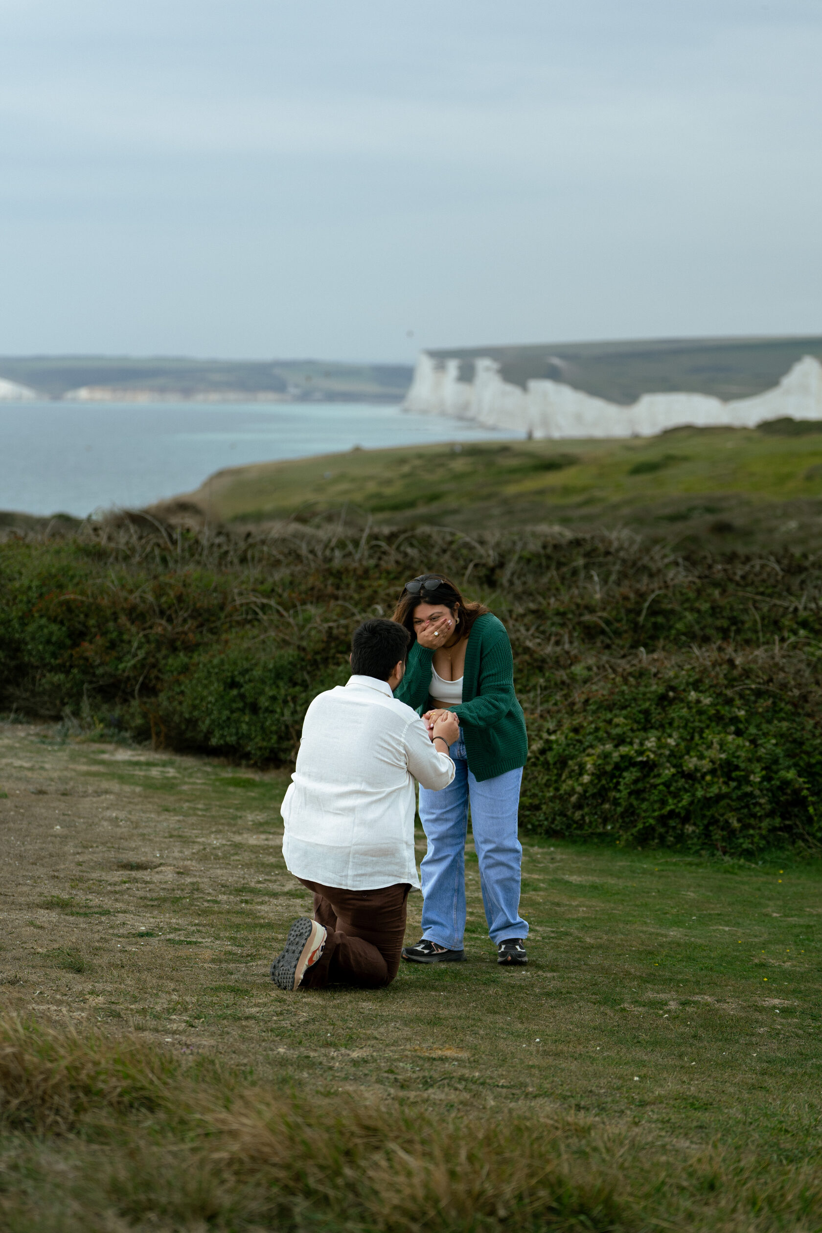Partner kneeling to propose with the Seven Sisters chalk cliffs in the distance