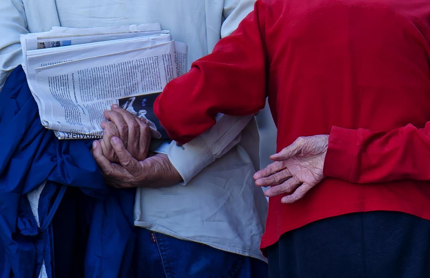 Close-up of elderly hands holding a newspaper against a red jacket.