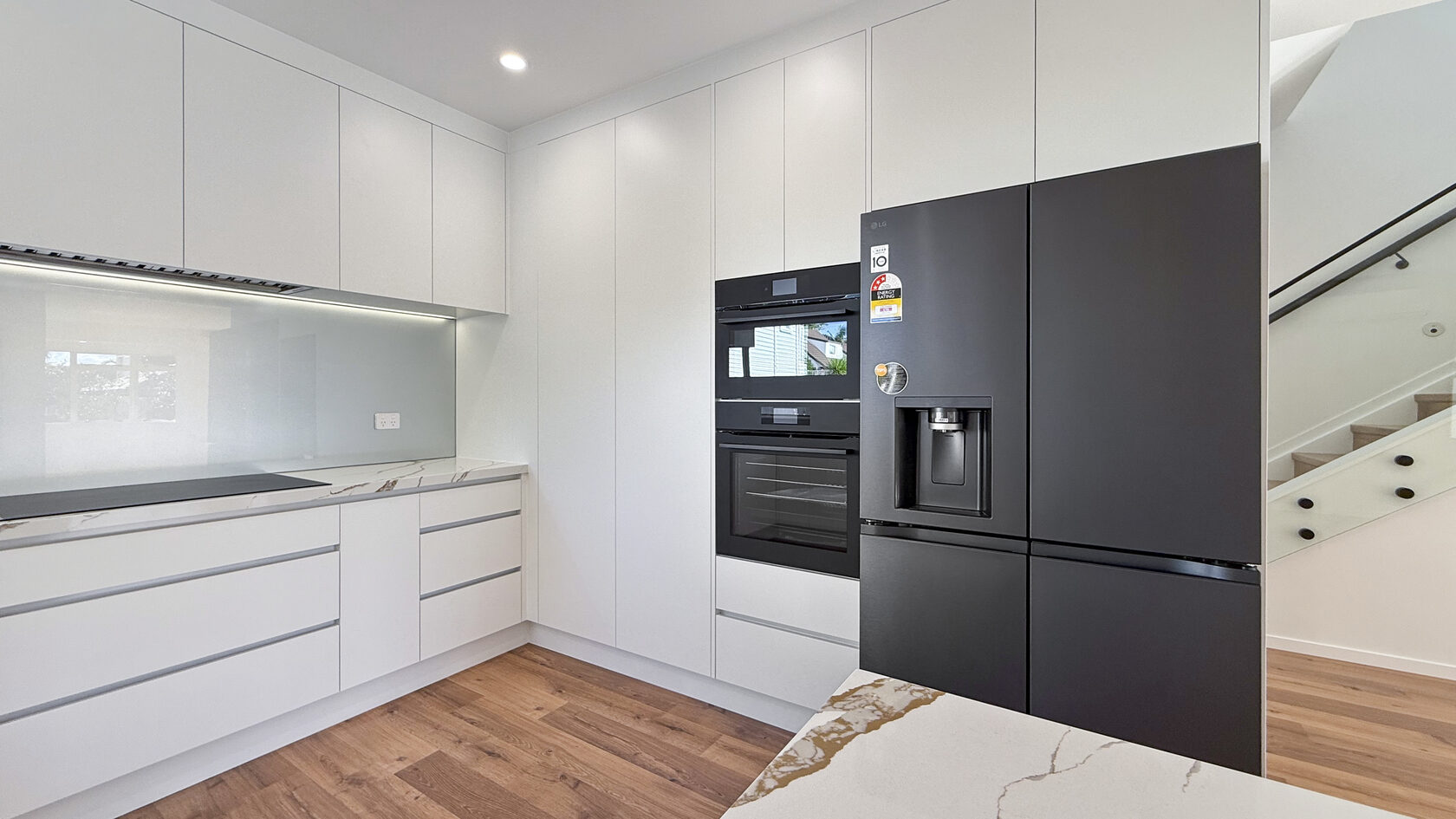 Floor-to-ceiling white kitchen cabinetry with integrated black appliances in St Heliers.