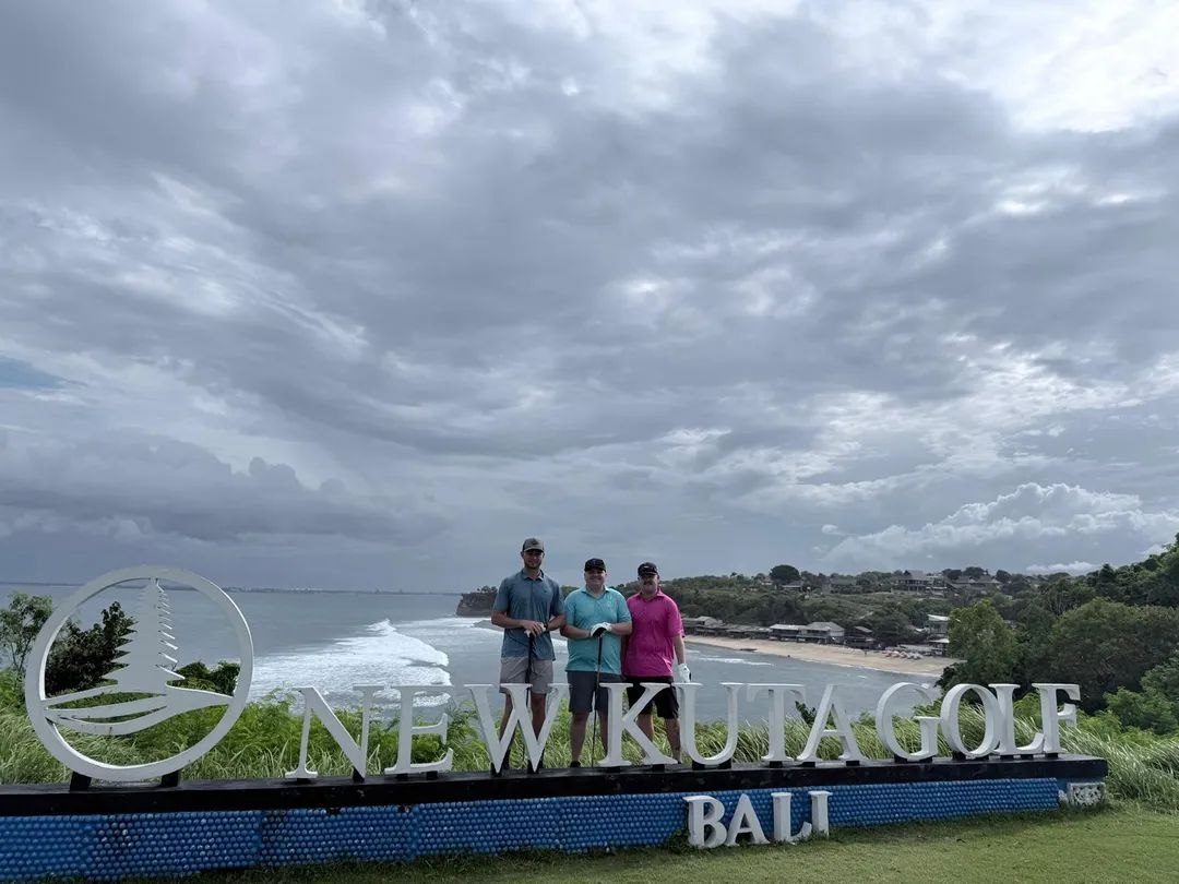 Three golfers at the New Kuta Golf sign above the Pecatu cliffs