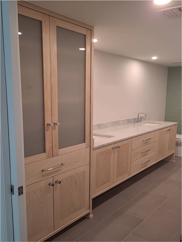 Custom bathroom vanity with double sinks, marble countertop and tall storage cabinet in pickled white oak