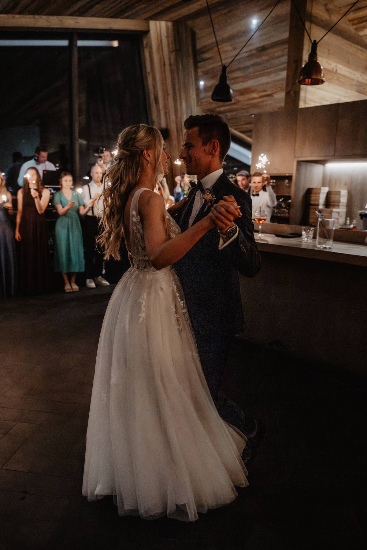 Bride and groom sharing their first dance at a cozy mountain lodge reception, guests watching
