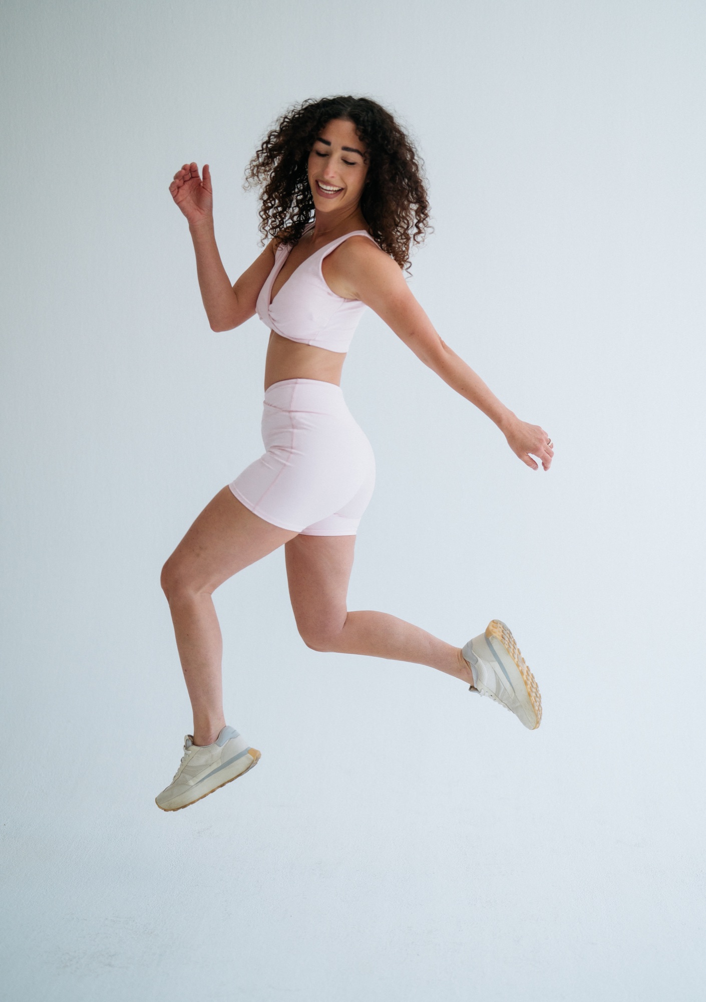 Model in hellrosa Sportkleidung und Sneakers im Sprung vor hellem Hintergrund
