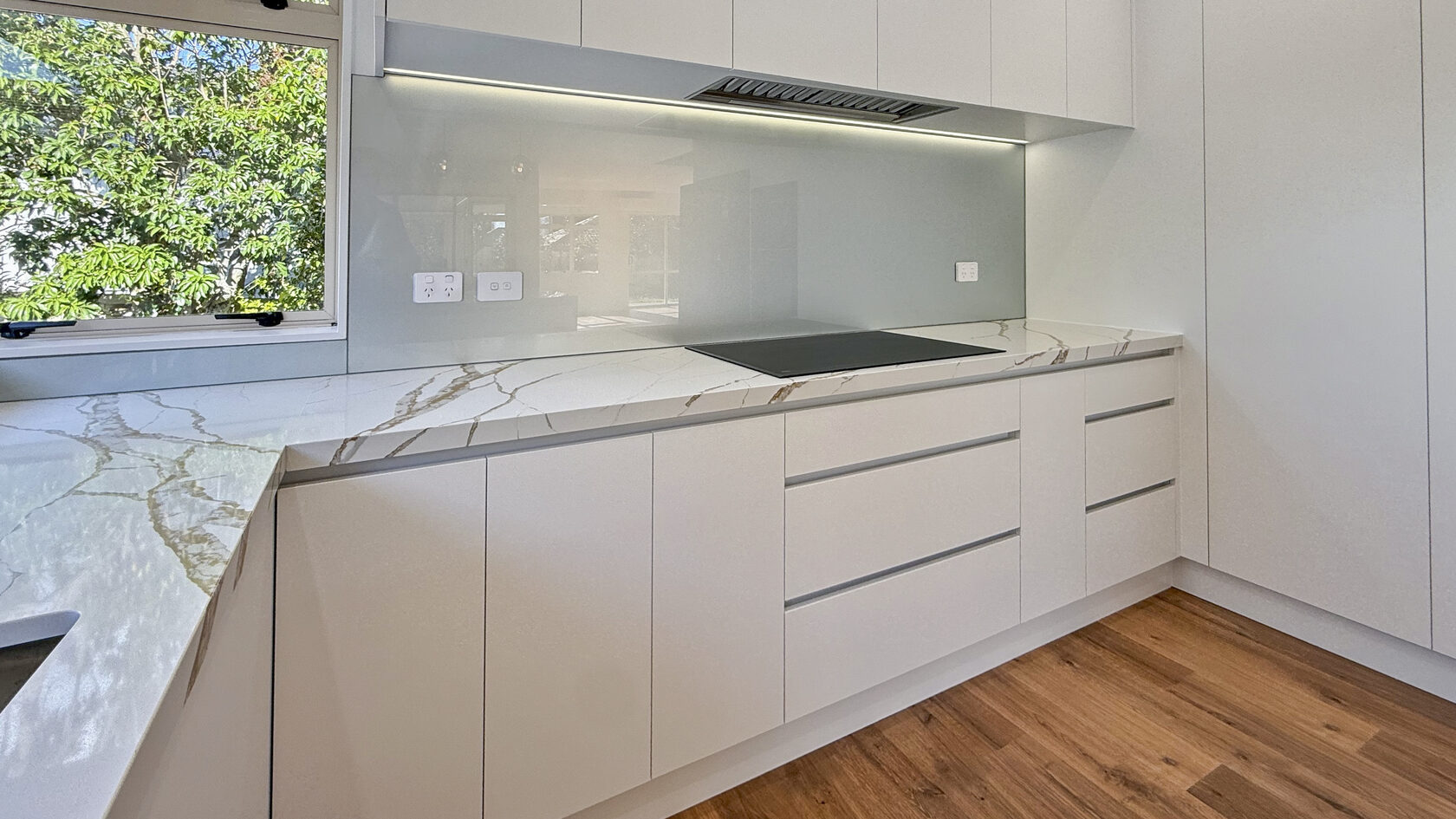 Modern St Heliers kitchen with handleless white cabinetry and marble-look stone benchtops.