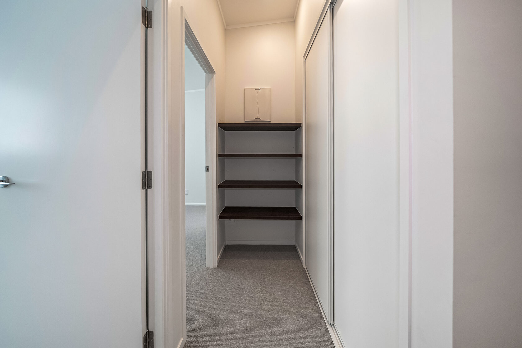 Hallway storage area with built-in timber shelves and sliding wardrobe doors.