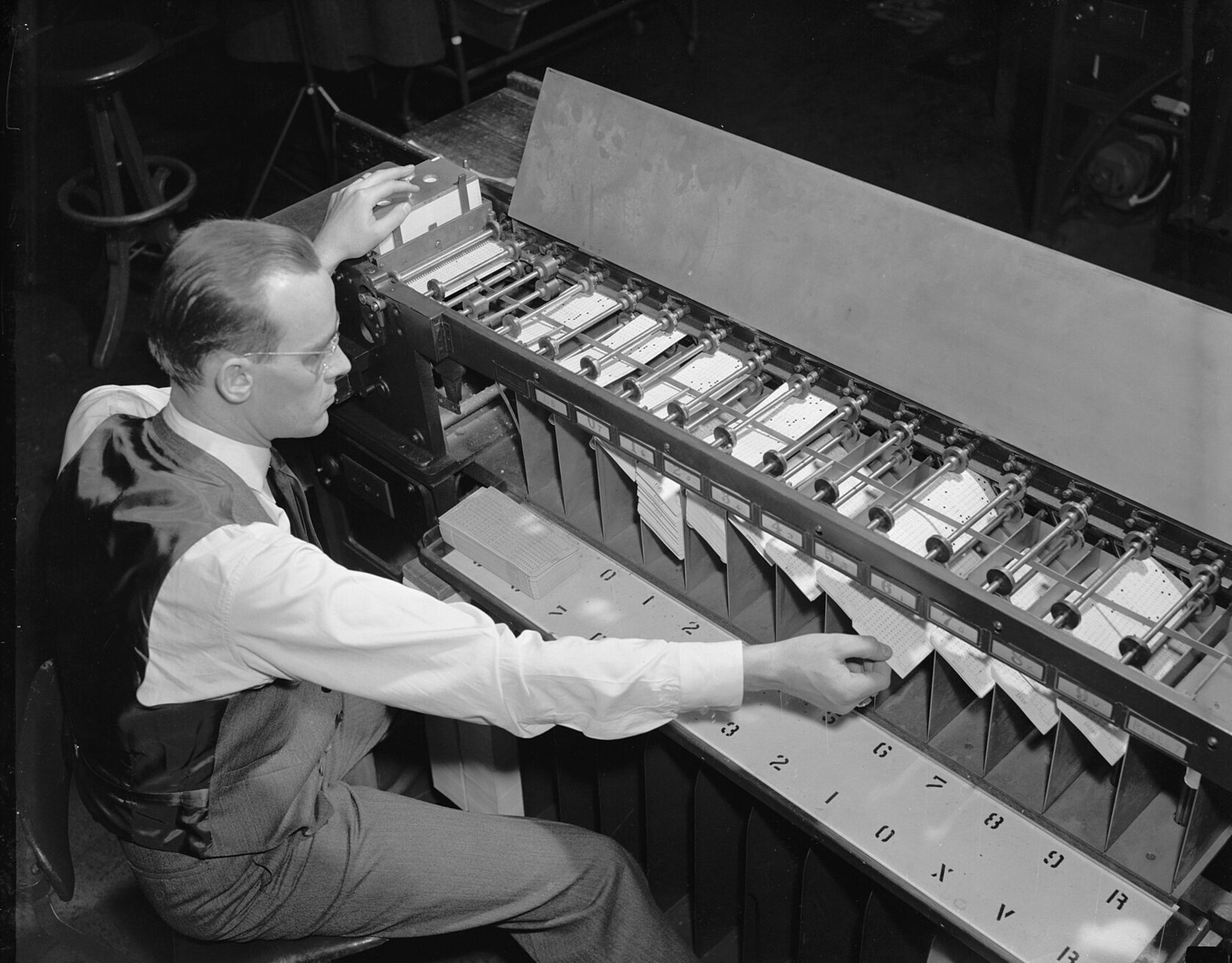 Archive photograph from about 1940: a man at a card sorter, punched cards dropping into numbered pockets