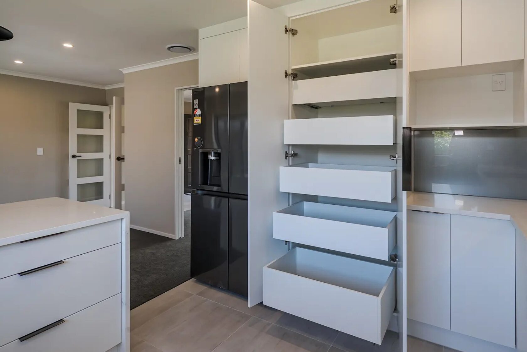After: Open kitchen pantry with pull-out white storage drawers beside a black refrigerator