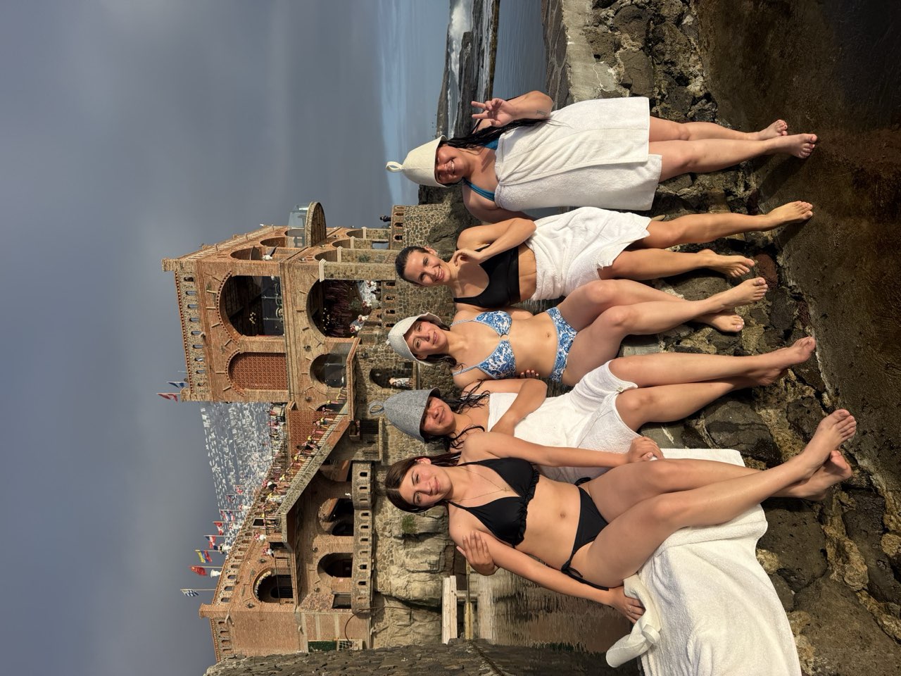 Un grupo de amigas con gorros de banya en las rocas frente al castillo